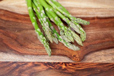 Kırsal ahşap bir yüzeye dizilmiş bir sürü taze kuşkonmaz mızrağı. Canlı yeşil renk ve detaylı doku bunu mutfak ve organik gıda kavramları için mükemmel bir görüntü yapıyor..