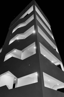 Modern Gece Binası, geometrik desenleri ve parlak ışıkları olan modern bir binanın düşük açılı görüntüsü, geceleri siyah ve beyaz olarak çekiliyor..