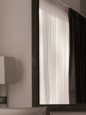 Pencereli, perdeli ve hafif ışıklandırmalı bir otel odası.