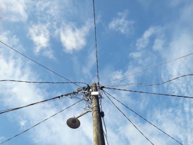 Gökyüzünün altında halat kabloları olan elektrik direkleri, elektrik direklerinde yerleşim yerlerine giden elektrik kabloları..