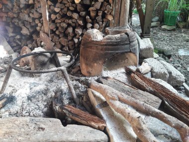 Endonezya kırsal mutfağında odun sobasında geleneksel bir çaydanlık. Dağınık odun ve küller otantik ve doğal kırsal yaşam atmosferini tamamlıyor..