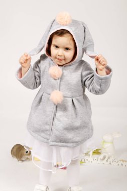 Yumuşak pastel tavşan kostümü giymiş, yumuşak kulaklı ve pofuduk ponponlu neşeli bir bebek ellerini kaldırmış, neşe ve neşe ifade ediyor. Paskalya için mükemmel