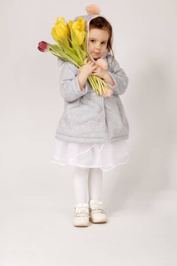 Yumuşak pastel tavşan kostümü giymiş yumuşak kulaklı ve pofuduk ponponlu bir çocuk elinde bir buket taze sarı ve bordo lale tutuyor. Paskalya için mükemmel