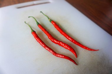 Kahverengi ahşap arka planda izole edilmiş plastik bir doğrama tahtasındaki kırmızı biberler.