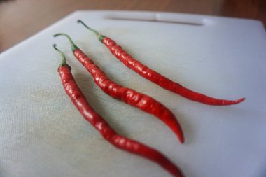 Kahverengi ahşap arka planda izole edilmiş plastik bir doğrama tahtasındaki kırmızı biberler.