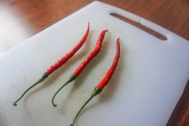 Kahverengi ahşap arka planda izole edilmiş plastik bir doğrama tahtasındaki kırmızı biberler.