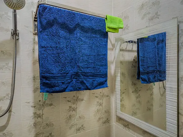 Mavi havlu banyodaki tırabzanda asılı aynadaki yansımasıyla.