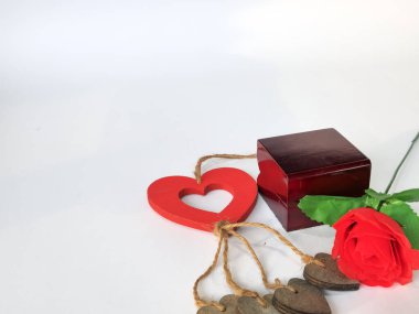 Yapay bir gül sapı, yüzük kutusu ve beyaz arka planda izole edilmiş kalp şeklinde ahşap bir süs.