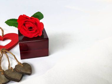 Yapay bir gül sapı, yüzük kutusu ve beyaz arka planda izole edilmiş kalp şeklinde ahşap bir süs.