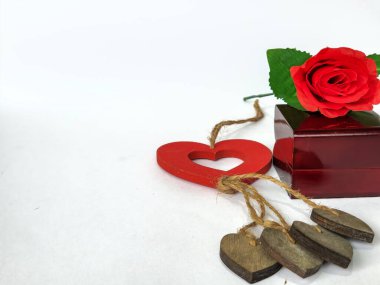 Yapay bir gül sapı, yüzük kutusu ve beyaz arka planda izole edilmiş kalp şeklinde ahşap bir süs.