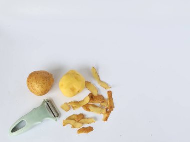 Kabuğu soyulmuş patates ve soyulmamış patatesli soyucu beyaz arka planda izole edilmiş.