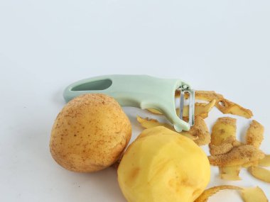 Kabuğu soyulmuş patates ve soyulmamış patatesli soyucu beyaz arka planda izole edilmiş.