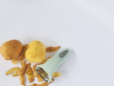 Kabuğu soyulmuş patates ve soyulmamış patatesli soyucu beyaz arka planda izole edilmiş.