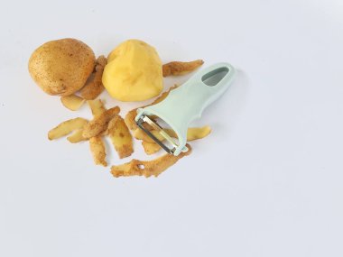 Kabuğu soyulmuş patates ve soyulmamış patatesli soyucu beyaz arka planda izole edilmiş.