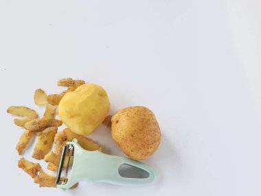 Kabuğu soyulmuş patates ve soyulmamış patatesli soyucu beyaz arka planda izole edilmiş.