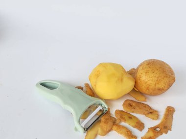 Kabuğu soyulmuş patates ve soyulmamış patatesli soyucu beyaz arka planda izole edilmiş.