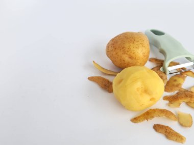 Kabuğu soyulmuş patates ve soyulmamış patatesli soyucu beyaz arka planda izole edilmiş.