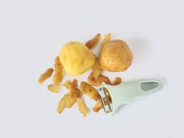 Kabuğu soyulmuş patates ve soyulmamış patatesli soyucu beyaz arka planda izole edilmiş.