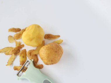 Kabuğu soyulmuş patates ve soyulmamış patatesli soyucu beyaz arka planda izole edilmiş.
