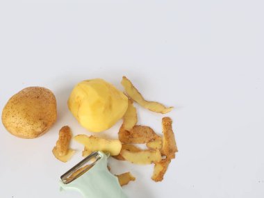 Kabuğu soyulmuş patates ve soyulmamış patatesli soyucu beyaz arka planda izole edilmiş.