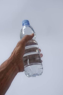 Beyaz arka planda plastik ambalajda bir şişe maden suyu tutan el.