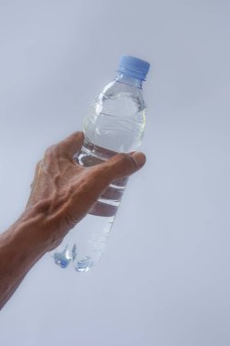 Beyaz arka planda plastik ambalajda bir şişe maden suyu tutan el.