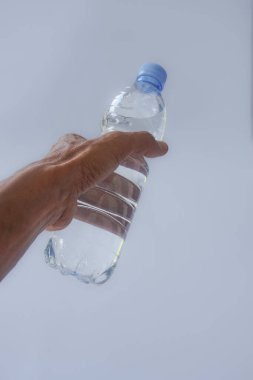 Beyaz arka planda plastik ambalajda bir şişe maden suyu tutan el.