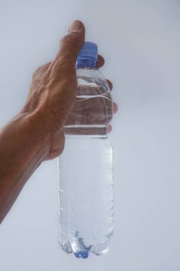Beyaz arka planda plastik ambalajda bir şişe maden suyu tutan el.