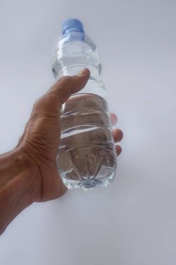 Beyaz arka planda plastik ambalajda bir şişe maden suyu tutan el.