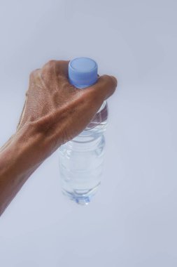 Beyaz arka planda plastik ambalajda bir şişe maden suyu tutan el.