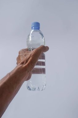 Beyaz arka planda plastik ambalajda bir şişe maden suyu tutan el.