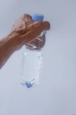 Beyaz arka planda plastik ambalajda bir şişe maden suyu tutan el.