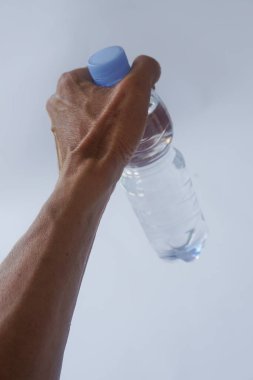 Beyaz arka planda plastik ambalajda bir şişe maden suyu tutan el.