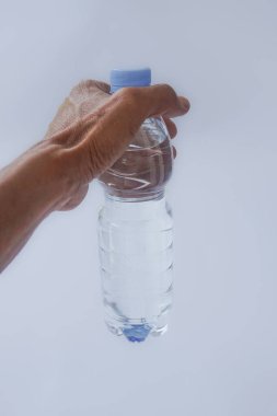 Beyaz arka planda plastik ambalajda bir şişe maden suyu tutan el.