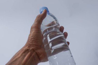 Beyaz arka planda plastik ambalajda bir şişe maden suyu tutan el.