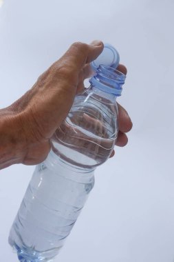 Beyaz arka planda plastik ambalajda bir şişe maden suyu tutan el.