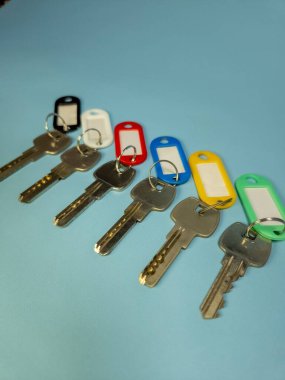 Açık mavi arkaplanda izole edilmiş renkli anahtarlıklara sahip birkaç anahtar.