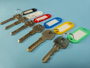 Açık mavi arkaplanda izole edilmiş renkli anahtarlıklara sahip birkaç anahtar.