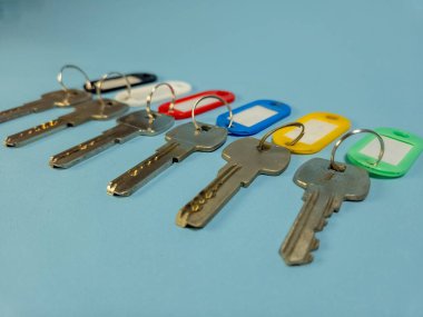 Açık mavi arkaplanda izole edilmiş renkli anahtarlıklara sahip birkaç anahtar.