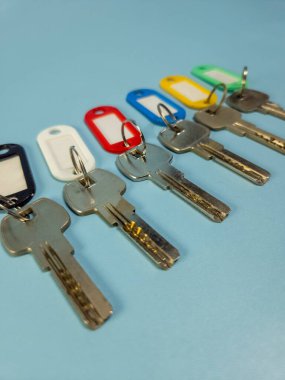 Açık mavi arkaplanda izole edilmiş renkli anahtarlıklara sahip birkaç anahtar.