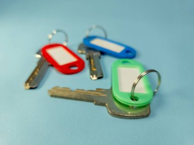 Açık mavi arkaplanda izole edilmiş renkli anahtarlıklara sahip birkaç anahtar.