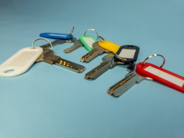 Açık mavi arkaplanda izole edilmiş renkli anahtarlıklara sahip birkaç anahtar.