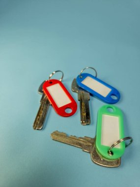 Açık mavi arkaplanda izole edilmiş renkli anahtarlıklara sahip birkaç anahtar.