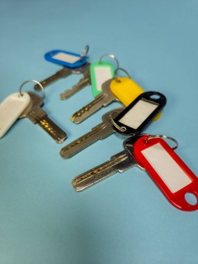 Açık mavi arkaplanda izole edilmiş renkli anahtarlıklara sahip birkaç anahtar.