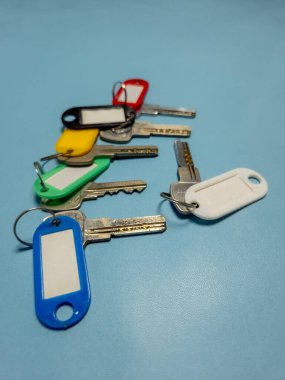 Açık mavi arkaplanda izole edilmiş renkli anahtarlıklara sahip birkaç anahtar.
