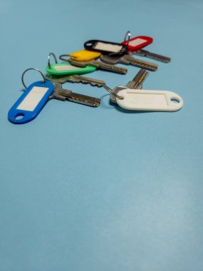 Açık mavi arkaplanda izole edilmiş renkli anahtarlıklara sahip birkaç anahtar.