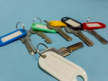 Açık mavi arkaplanda izole edilmiş renkli anahtarlıklara sahip birkaç anahtar.