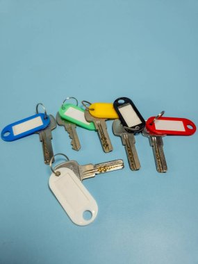 Açık mavi arkaplanda izole edilmiş renkli anahtarlıklara sahip birkaç anahtar.