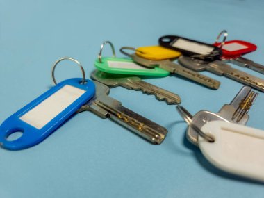 Açık mavi arkaplanda izole edilmiş renkli anahtarlıklara sahip birkaç anahtar.