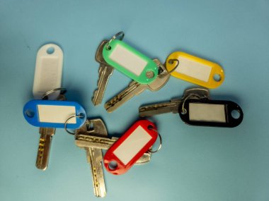 Açık mavi arkaplanda izole edilmiş renkli anahtarlıklara sahip birkaç anahtar.